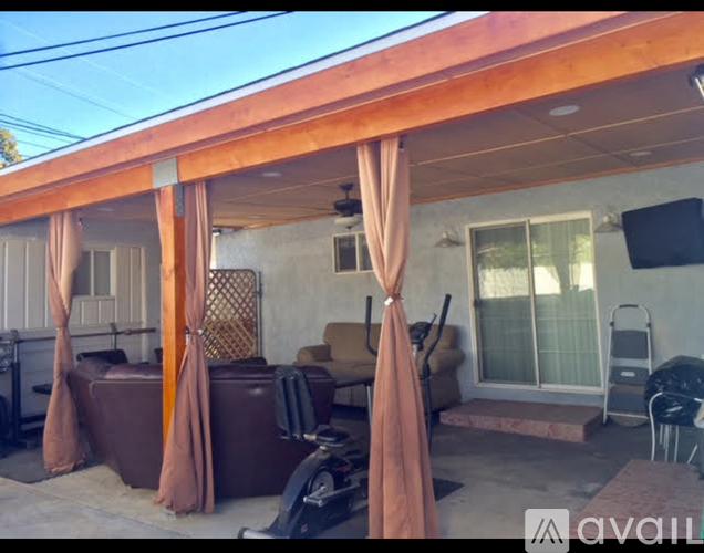 A patio with a brown couch, chairs, and a table under a wooden pergola.