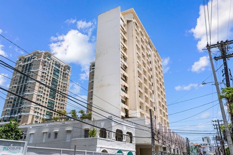 A white building with a green stripe on the bottom is in the foreground with a blue sky and clouds in the background.