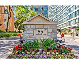 A stone sign with the number 55 and the words Elm Drive West is surrounded by flowers.