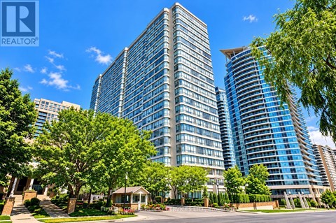 A tall building with a glass facade stands in front of a smaller building and trees.