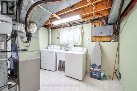 A small, unfinished basement with a washer and dryer, a desk, and a surfboard.