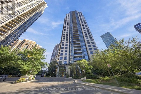 A tall building with a glass facade stands in the middle of a city street.