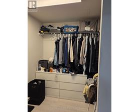 A closet with clothes hanging and a black trash bin.