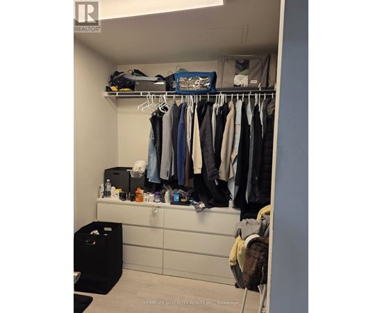 A closet with clothes hanging and a black trash bin.