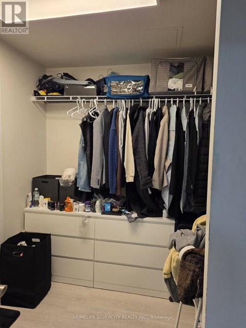 A closet with clothes hanging and a black trash bin.