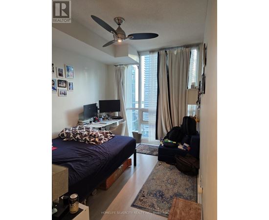 A bedroom with a bed, a fan, a couch, and a television.