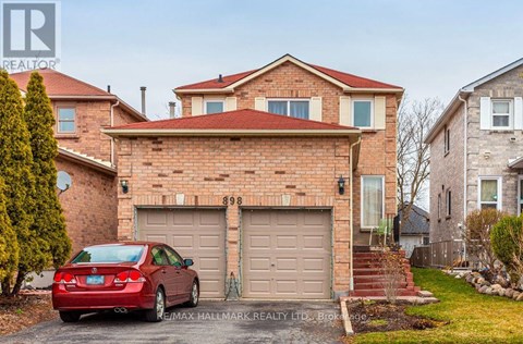 A red car is parked in front of a brick house with a garage.