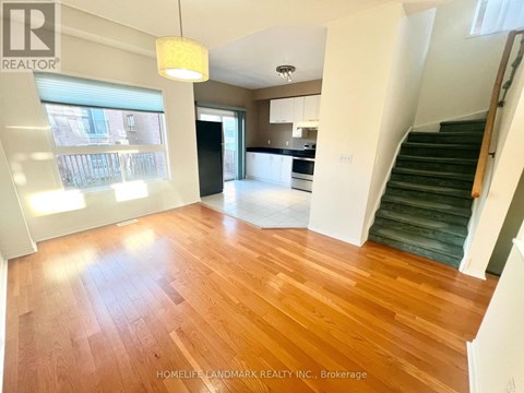 A brightly lit living room with wooden floors and a staircase leading to the upper level.