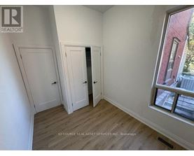 A room with white walls and wooden flooring, with a window showing a red building outside.