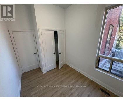 A room with white walls and wooden flooring, with a window showing a red building outside.