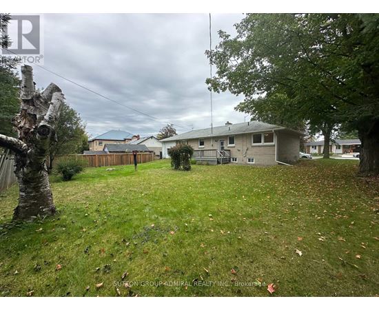 A backyard with a grassy area, a tree, and a house in the background.