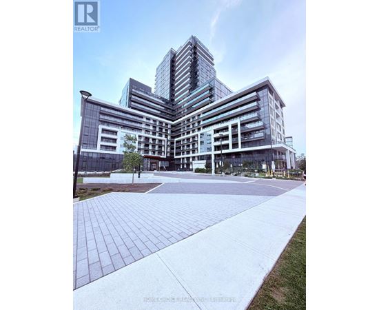 A modern multi-story building with a glass facade and a landscaped courtyard in front.