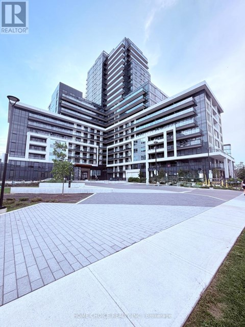 A modern multi-story building with a glass facade and a landscaped courtyard in front.