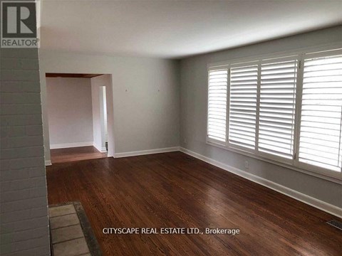 A room with wooden floors and white walls, with a window on the right side.