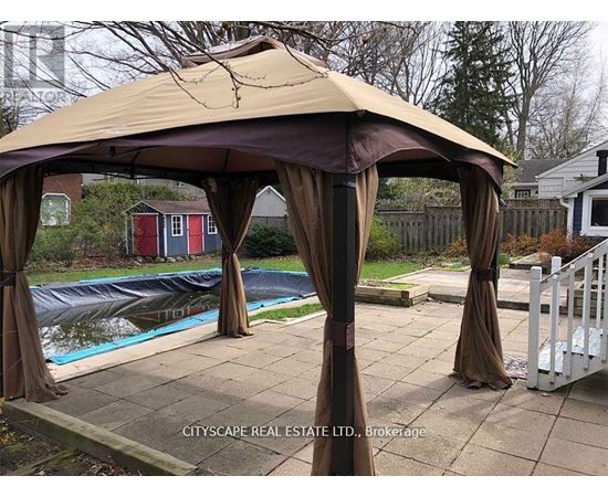A gazebo with brown drapes is set up in a backyard.