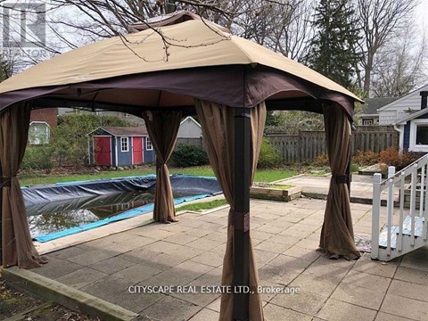 A gazebo with brown drapes is set up in a backyard.
