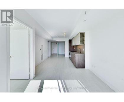 A spacious, white-walled hallway with a wooden floor and a white door on the left.