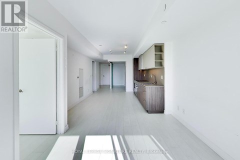 A spacious, white-walled hallway with a wooden floor and a white door on the left.