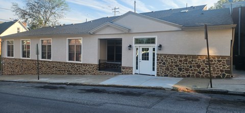 A small building with a white door and windows is surrounded by a stone wall.