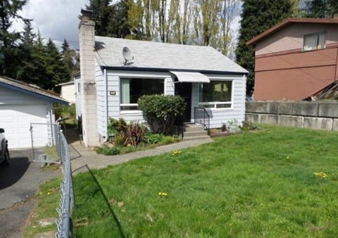 A small house with a grey roof and a white fence.