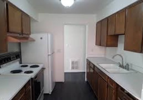 A kitchen with a white stove top oven, white refrigerator, brown cabinets, and a white sink.