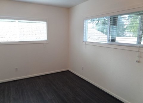 A room with two windows and dark wood flooring.