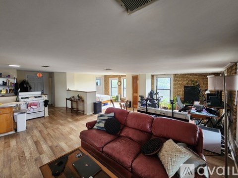 A red couch with a laptop on a wooden table in a room with a kitchen in the background.