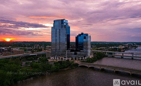 A sunset view of a cityscape with two prominent buildings and a river in the foreground.