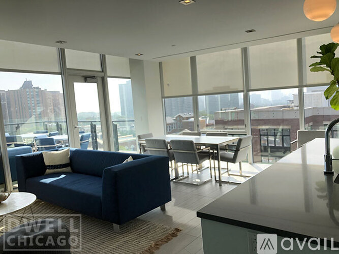 A blue couch is in the middle of a living room with a kitchen area in the background.