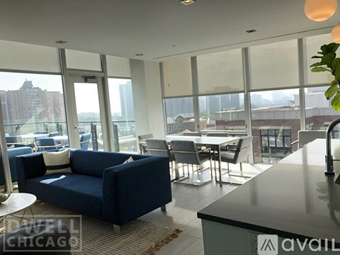 A blue couch is in the middle of a living room with a kitchen area in the background.