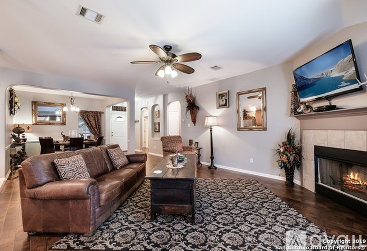 A living room with a brown leather couch, a fireplace, and a television mounted on the wall.