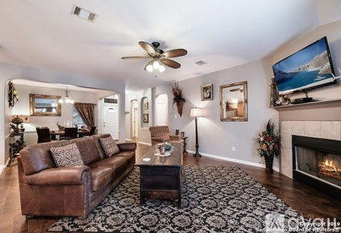 A living room with a brown leather couch, a fireplace, and a television mounted on the wall.