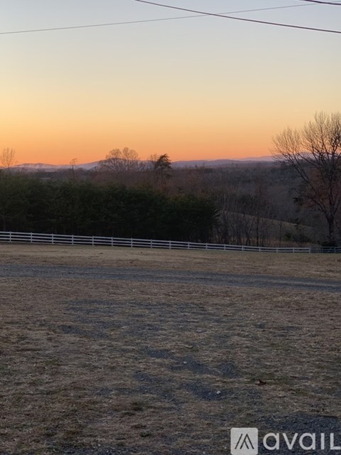 A field with a fence and trees in the distance during sunset.