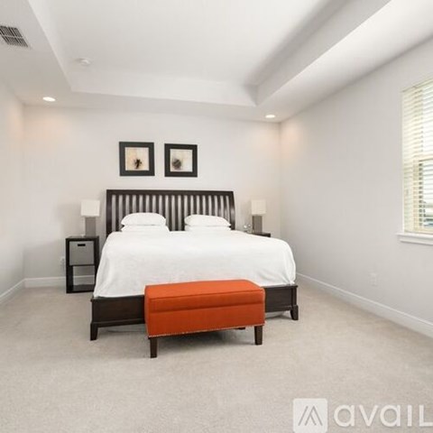 A bedroom with a large bed and a small orange ottoman.