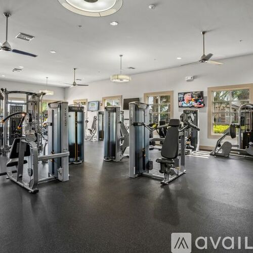 A well-equipped gym with various exercise machines and a ceiling fan.