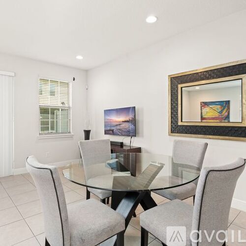 A dining room with a glass table and grey chairs.