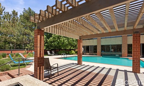 A pool area with a wooden pergola and a brick pillar.