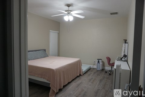A bedroom with a bed, chair, and fan.