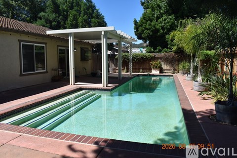 A pool in a backyard with a patio and a house in the background.