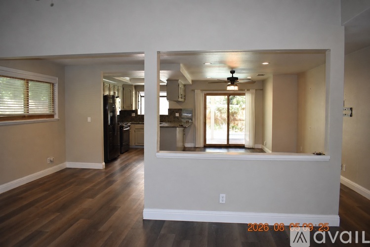 A spacious living room with a kitchen in the background and a window with blinds on the left.