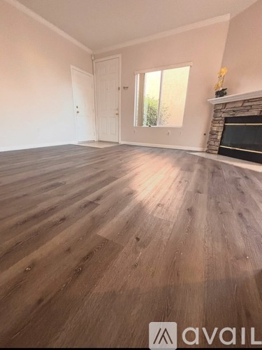 A room with wooden flooring and a fireplace with a window in the background.