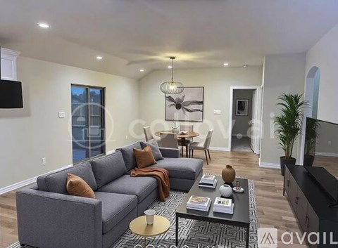 A modern living room with a grey sofa, a coffee table, and a flat-screen TV mounted on the wall.