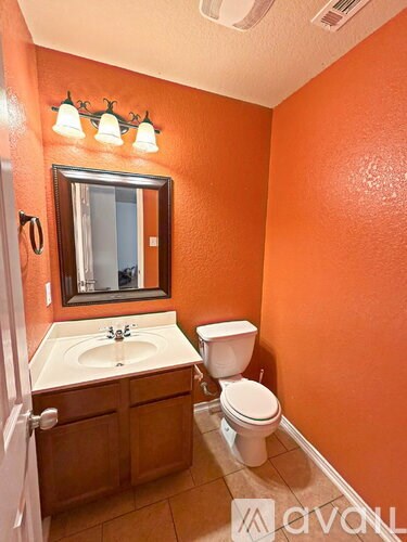 A bathroom with orange walls has a toilet, sink, and mirror.