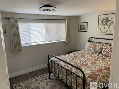 A bedroom with a bed, a window with curtains, and a framed picture of a bicycle on the wall.