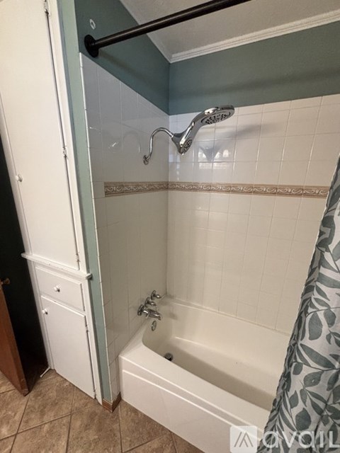A white bathtub with a shower head and a grey shower curtain.