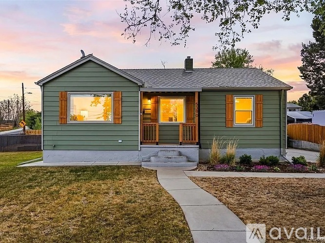 A small green house with a porch and a front yard.