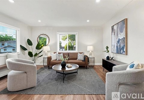 A living room with a grey sofa, a grey armchair, a grey chair, a coffee table, a rug, and a painting on the wall.