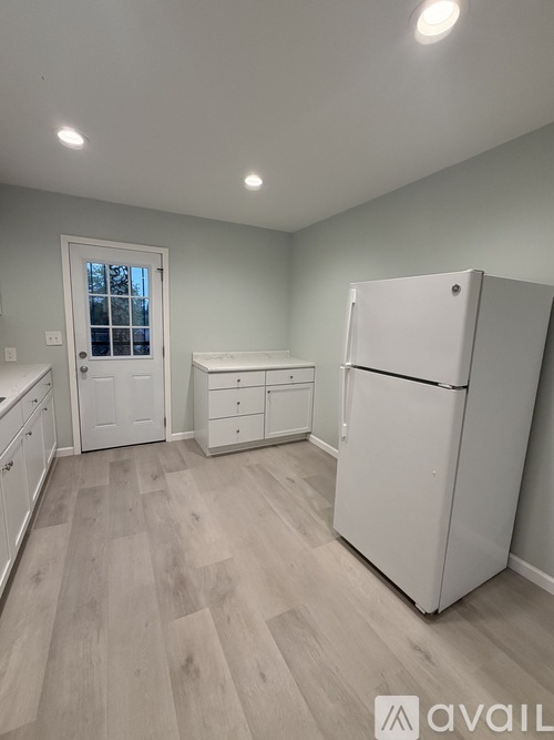 A kitchen with a white fridge, cabinets, and a door leading outside.