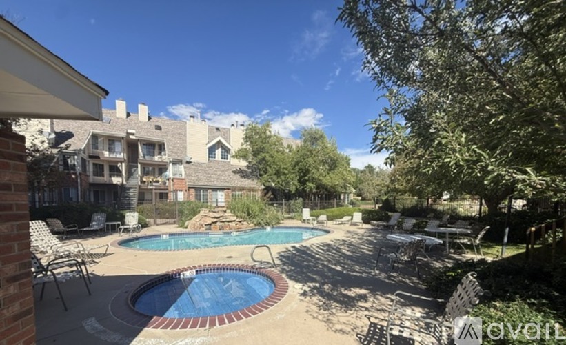 A pool surrounded by chairs and trees with houses in the background.