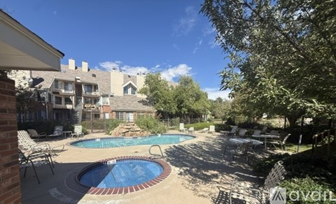 A pool surrounded by chairs and trees with houses in the background.